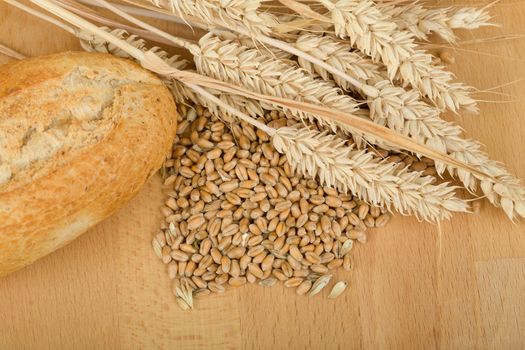 Freshly baked traditional roll on wooden table with ears of wheat grain