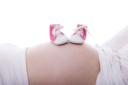 Little pink baby shoes on pregnant belly over white background