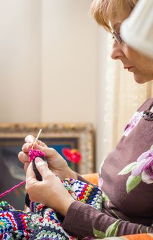 Portrait of senior woman knitting a vintage wool quilt with colorful patches