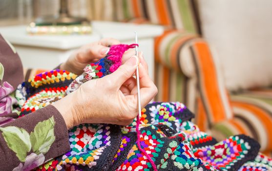 Hands of senior woman knitting a vintage wool quilt with colorful patches