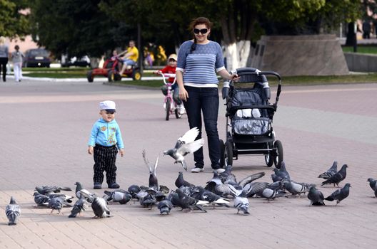 Unknown woman with a carriage on a walk with the child in the Park feeding the pigeons