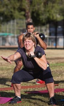 Strong middle aged woman squatting with kettle bell weights