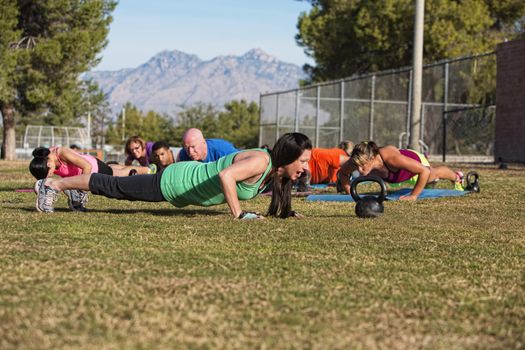 Young woman leading group in push up exercises outdoors