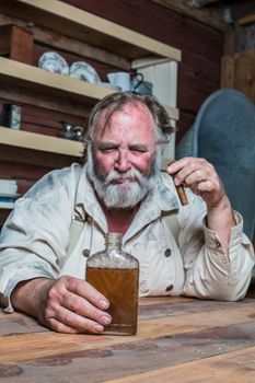 Unhappy Drunk Cigar Smoking Western Man Looks Towards His Drink as he Sits at Table