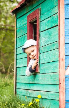 Boy plays in little 
toy wooden house outdoor