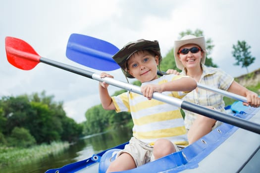 Happy young boy with mother paddling a kayak on the river, enjoying a lovely summer day