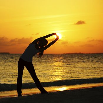 Yoga woman in serene sunset at beach doing stretching workout