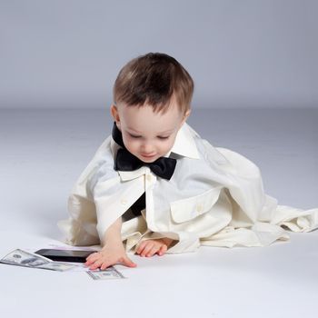 Boy toddler businessman sitting dressed in grown-shirt with bow tie, takes dollars out of the ground