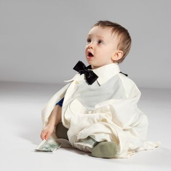 Boy toddler businessman sitting dressed in grown-shirt with bow tie, holding in hand the dollars