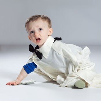 Boy toddler businessman sitting dressed in grown-shirt with bow tie, takes dollars out of the ground