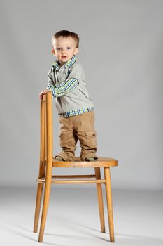 Toddler boy standing on a big wooden chair