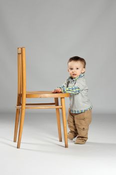 Toddler boy standing beside a big wooden chair
