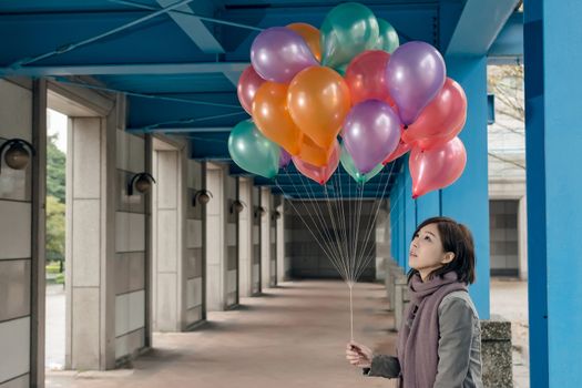 Elegant Asian beauty holding balloons under bridge in city.