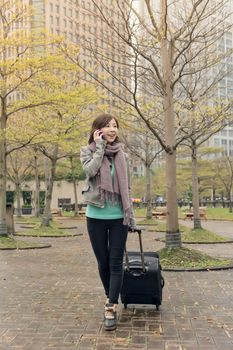 Attractive Asian woman holding suitcase and talking on phone at street, Taipei, Taiwan.