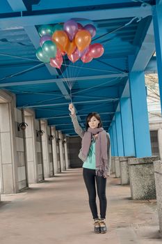 Elegant Asian beauty holding balloons under bridge in city.