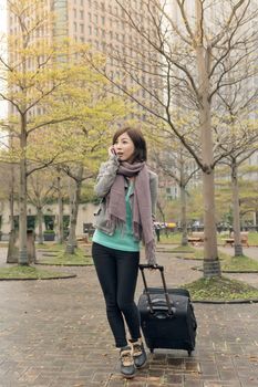 Attractive Asian woman holding suitcase and talking on phone at street, Taipei, Taiwan.