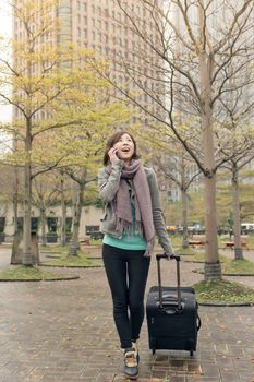 Attractive Asian woman holding suitcase and talking on phone at street, Taipei, Taiwan.