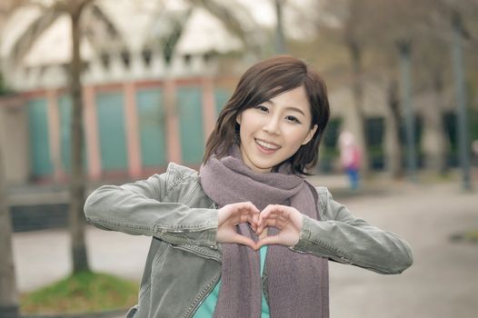 Attractive young woman showing a love shape gesture in the park, Taipei, Taiwan.