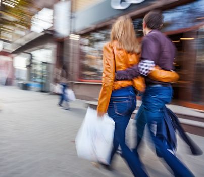 Man in jeans and a woman in a leather jacket walking down the street hugging. Intentional motion blur