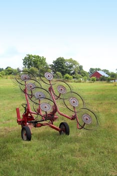 A hay rake sitting in an empty farm field.