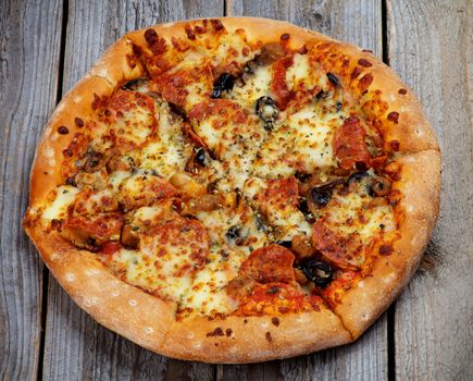 Freshly Baked Pepperoni Pizza with Black Olives, Cheese and Spices on Rustic Wooden background