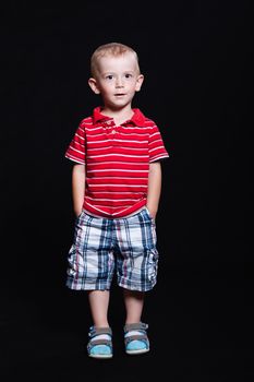 Little boy in a striped shirt and checkered shorts standing with hands in pockets