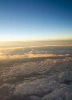 Aerial view of a cloudy sunrise while flying above the clouds. 