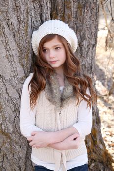 Winter girl leaning against a large tree 