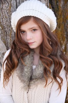 Winter girl leaning against a large tree 