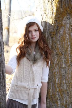 Winter girl leaning against a large tree 