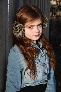 Red haired girl wearing earmuffs against wooden background 