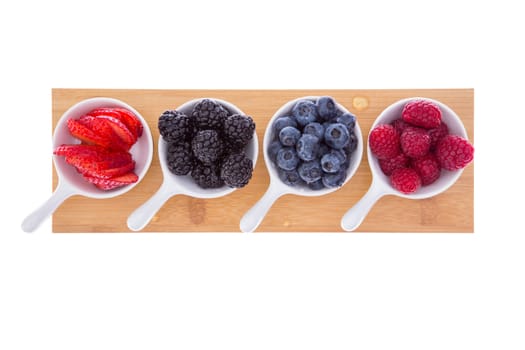 Variety of fresh ripe autumn berries served in small ceramic ramekins for a healthy refreshment of strawberries, raspberries, blueberries, and blackberries on a wooden board isolated on white