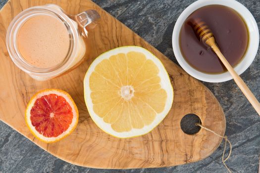 Freshly squeezed grapefruit juice served with a container of honey and two halved grapefruit on an old olivewood chopping board for a healthy breakfast, overhead view