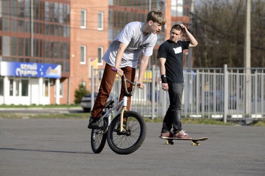 Two young guys are riding the bike and skateboard