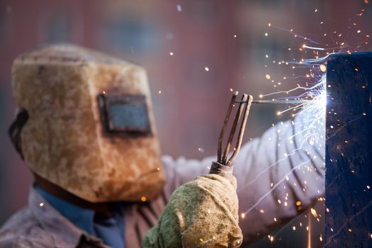 Heavy industry welder worker in protective mask hand holding arc welding torch working on metal construction