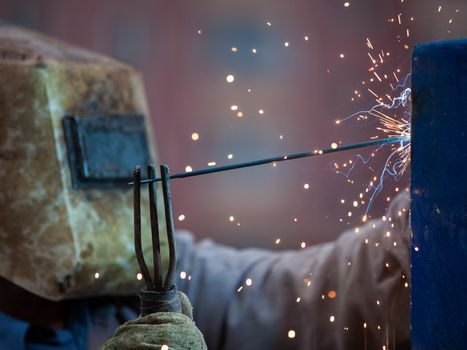 Heavy industry welder worker in protective mask hand holding arc welding torch working on metal construction