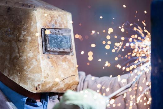 Heavy industry welder worker in protective mask hand holding arc welding torch working on metal construction