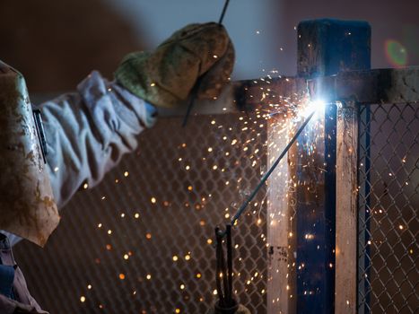 Heavy industry welder worker in protective mask hand holding arc welding torch working on metal construction