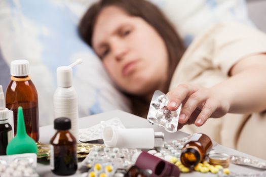 Adult woman patient hand holding vitamin pills lying down bed for cold and flu illness relief
