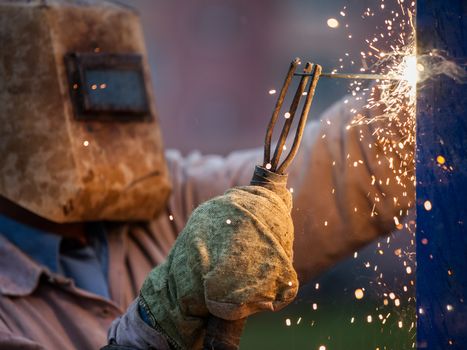 Heavy industry welder worker in protective mask hand holding arc welding torch working on metal construction