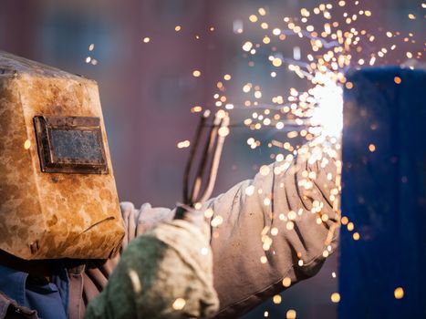 Heavy industry welder worker in protective mask hand holding arc welding torch working on metal construction