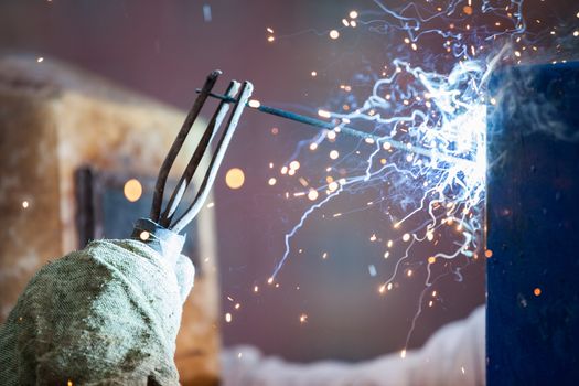 Heavy industry welder worker in protective mask hand holding arc welding torch working on metal construction