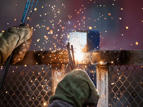 Heavy industry welder worker in protective mask hand holding arc welding torch working on metal construction