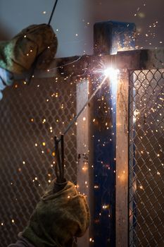 Heavy industry welder worker in protective mask hand holding arc welding torch working on metal construction