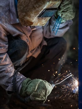 Heavy industry welder worker in protective mask hand holding arc welding torch working on metal construction