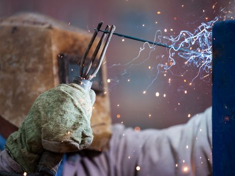 Heavy industry welder worker in protective mask hand holding arc welding torch working on metal construction