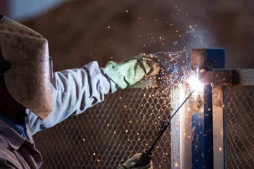 Heavy industry welder worker in protective mask hand holding arc welding torch working on metal construction
