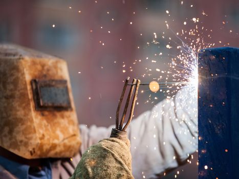 Heavy industry welder worker in protective mask hand holding arc welding torch working on metal construction