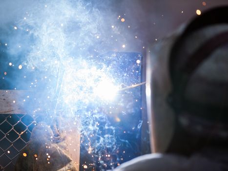 Heavy industry welder worker in protective mask hand holding arc welding torch working on metal construction