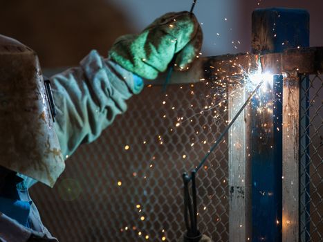 Heavy industry welder worker in protective mask hand holding arc welding torch working on metal construction